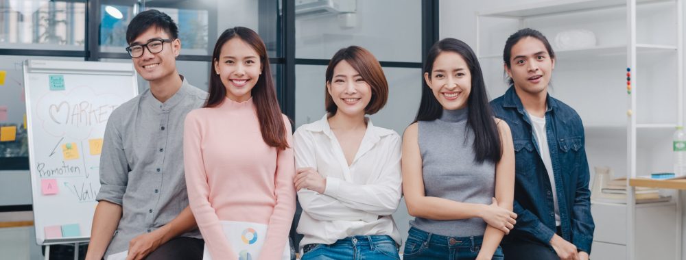 Group of Asia young creative people in smart casual wear looking at camera and smiling in creative office workplace. Diverse Asian male and female stand together at startup. Coworker teamwork concept.
