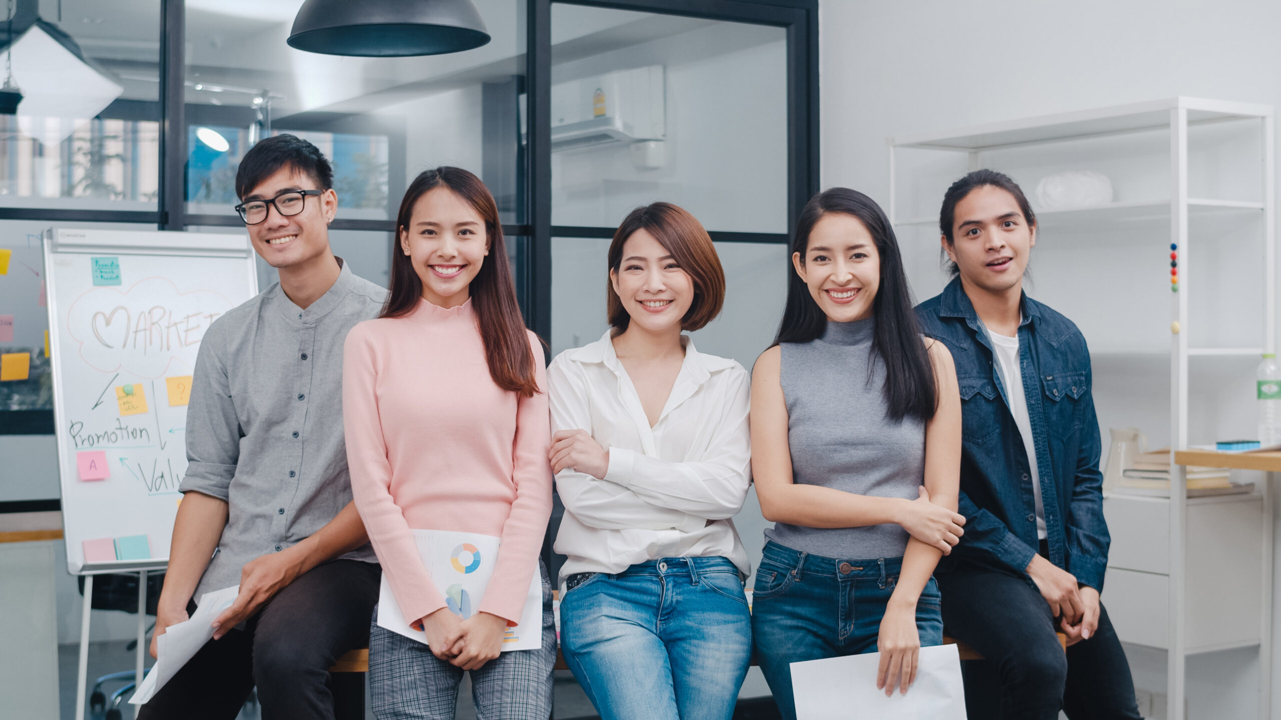 Group of Asia young creative people in smart casual wear looking at camera and smiling in creative office workplace. Diverse Asian male and female stand together at startup. Coworker teamwork concept.